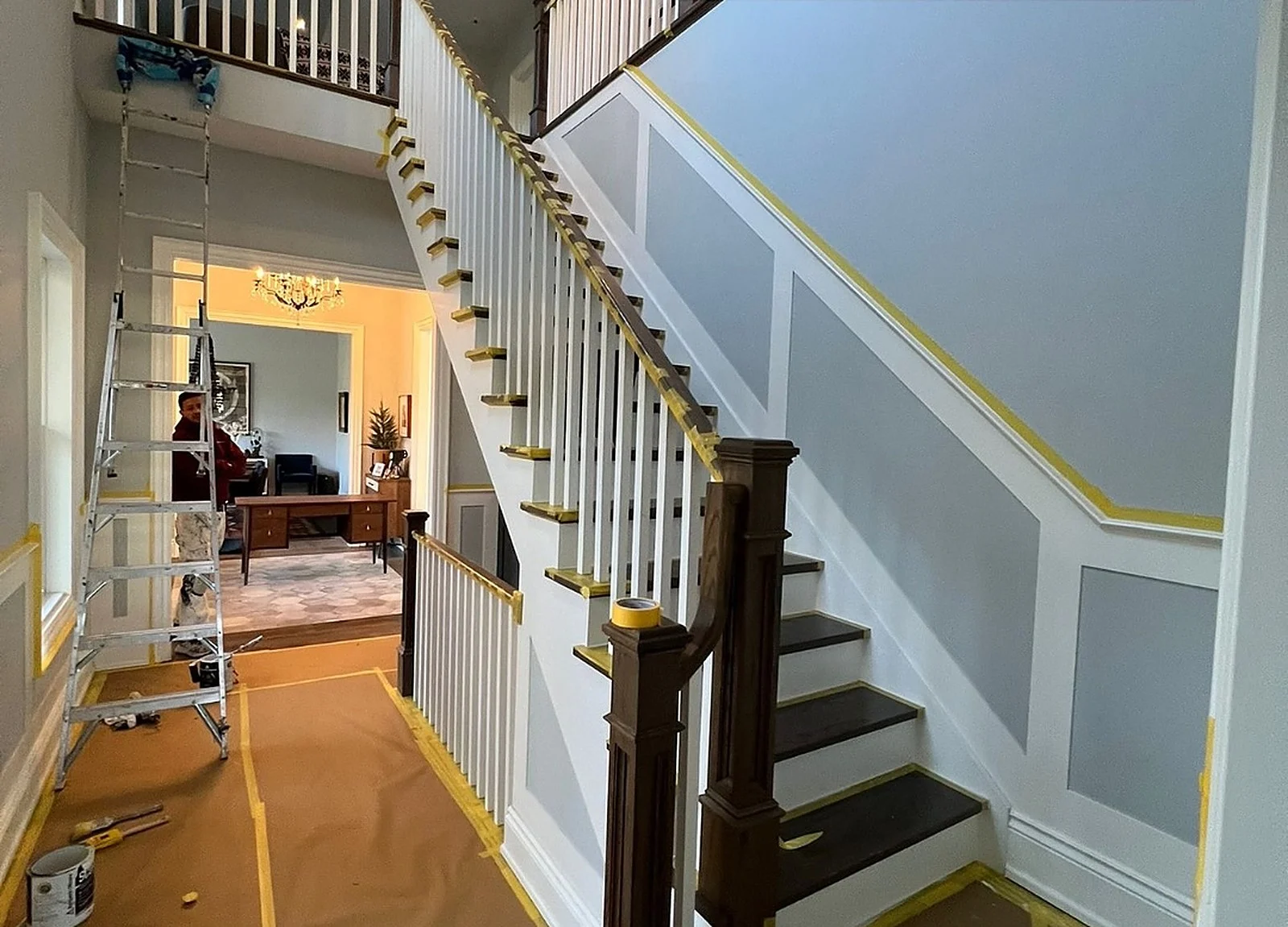 BEFORE: two-storey foyer staircase, white spindles, light blue walls with white wainscoting, ladder