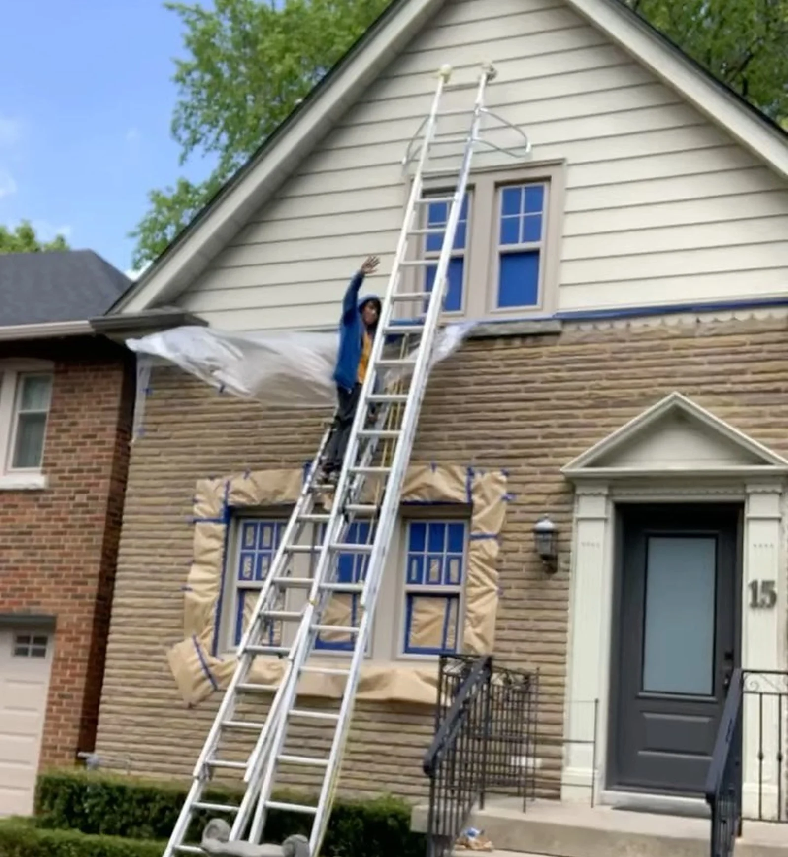 In progress: painter on tall ladder painting Forest Hill house gable siding