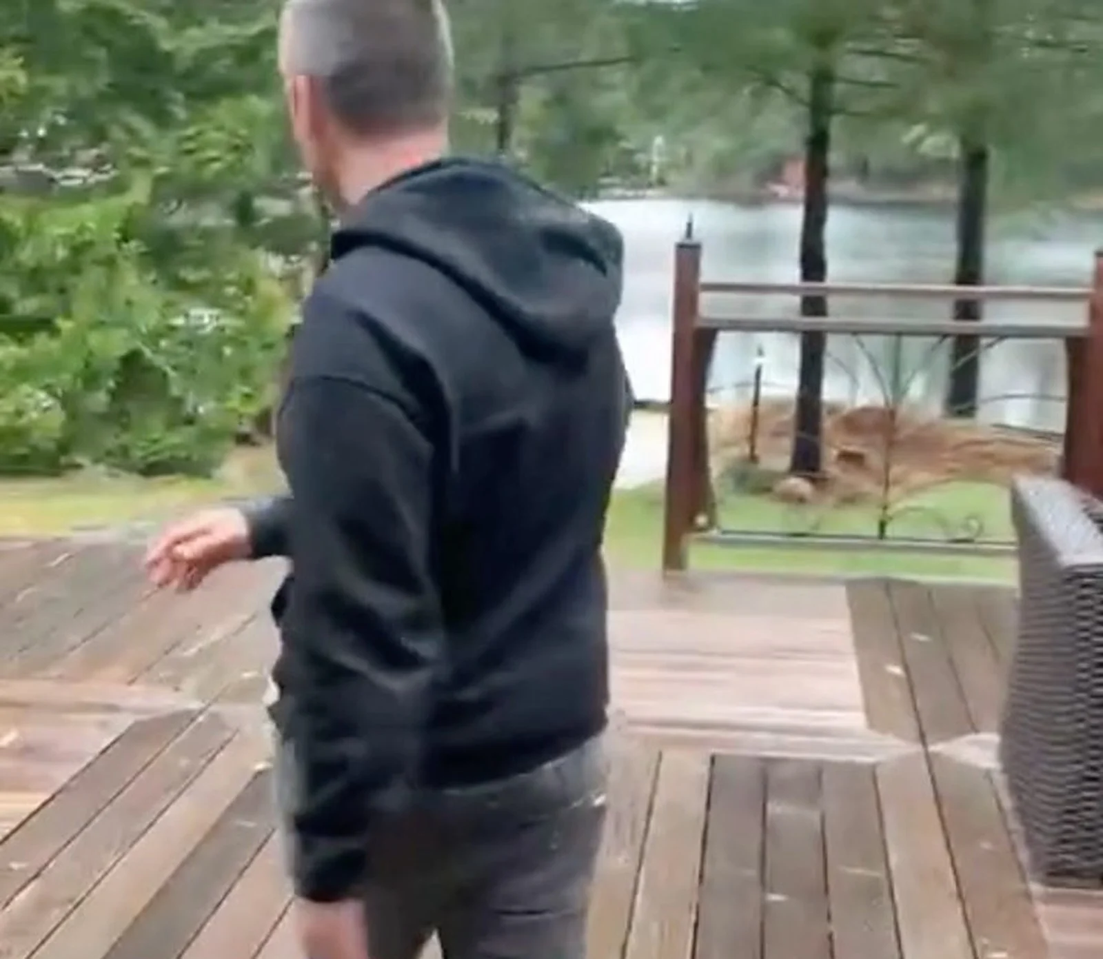 Man in black hoodie walking on cottage deck by lake (video still)
